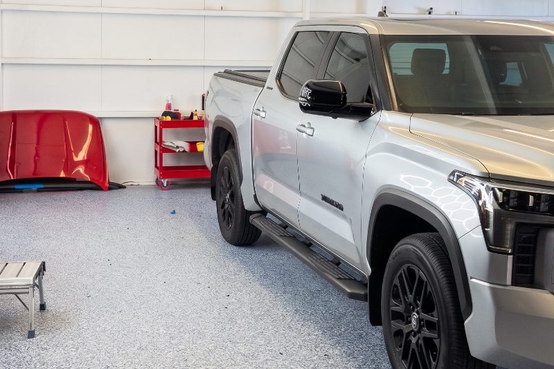 A silver pickup in the bay beside a removed red body panel propped against the wall