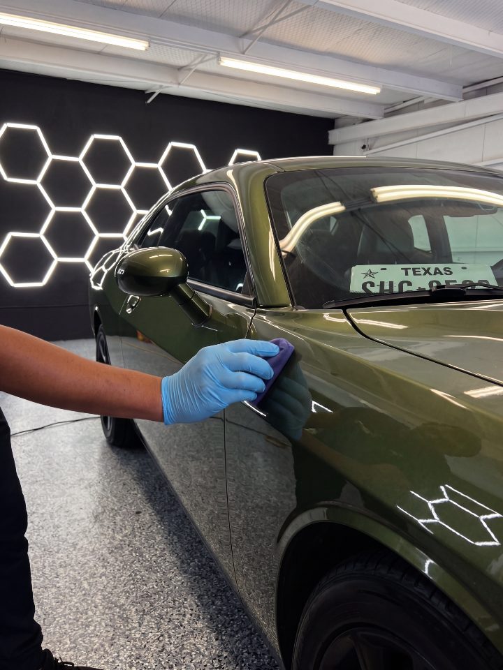 A gloved hand working a coating applicator across a green fender